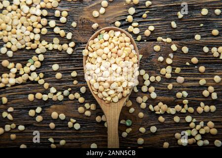 Trockene gelbe Erbsen in einem Löffel auf braunem Holz- Hintergrund. Bohnen für nahrhafte Suppe Stockfoto