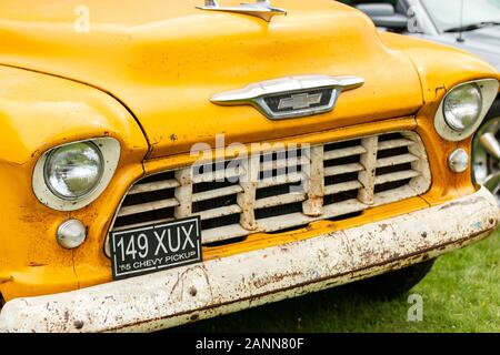 Nahaufnahme eines Vintage-gelben 1955 Chevy Pickups mit sichtbarem Rost und klassischem Design, der im Freien auf einer grasbewachsenen Fläche geparkt ist Stockfoto