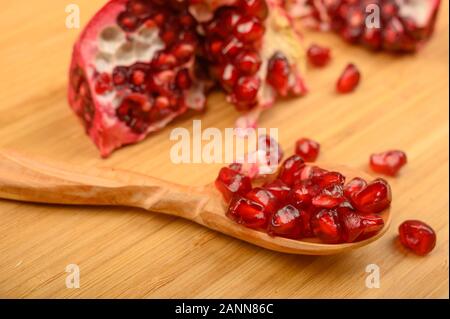 Brocken der Reife saftig Granatapfel und Granatapfel Samen auf einem Löffel aus Holz auf Holz Hintergrund. Nahaufnahme Stockfoto
