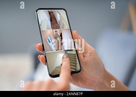 Nahaufnahme von einer Person Hand mit Home Security System auf Handy Stockfoto