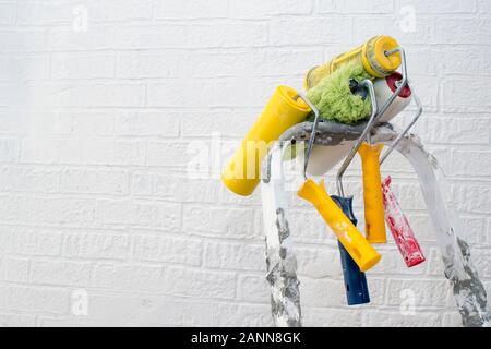 Aus lackiertem Metall Trittleiter close-up mit einem hängenden Set aus bunten Rollen auf dem Hintergrund einer weißen Wand. Stockfoto