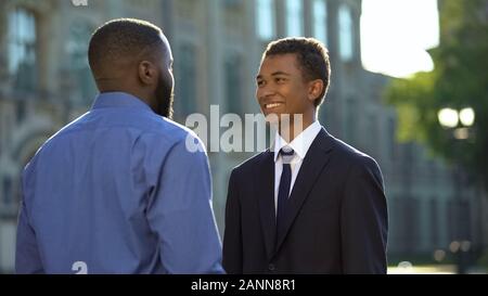 Afro-amerikanischen Vater gruss Sohn im Anzug im Freien Universität, Prom Feier Stockfoto