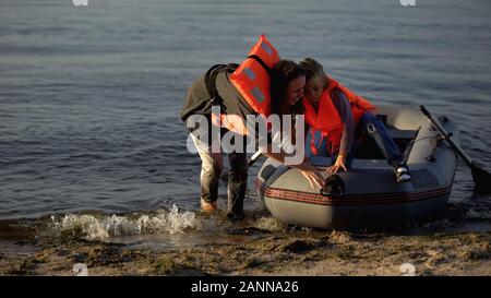 Mutter und Kind in Schwimmwesten aus dem Boot am Ufer, überlebte Schiffswrack Stockfoto