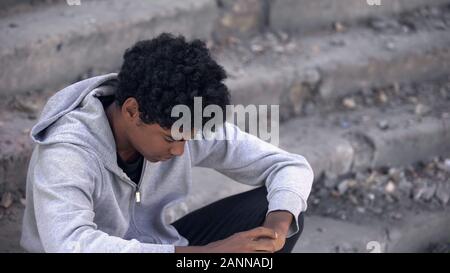 Verärgert afro-amerikanische Junge sitzt auf Treppe und denken über das Leben Probleme, Krieg Stockfoto