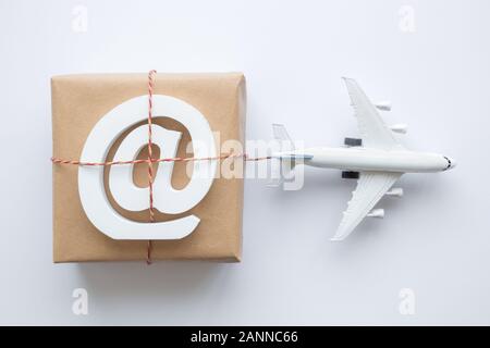 Flach von verpackten Paket mit e-Mail Symbol und Flugzeug Modell auf weißem Hintergrund. Versand Logistik Transport minimal kreatives Konzept. Stockfoto