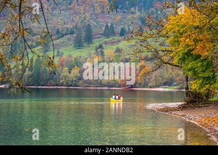 Touristen gehen für eine Kanutour rund um den See von Bohinj an einem schönen Tag im Herbst. Reisende Kajak auf das Ufer versteckt zwischen Bäumen, reflektiert in Stockfoto