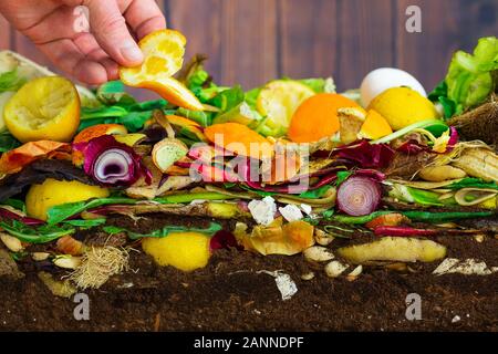 Männliche hand Hinzufügen einer Orangenschale zu einem bunten Komposthaufen bestehend aus verrottenden Küche Reste Stockfoto