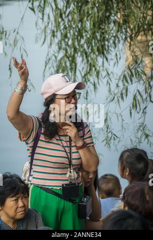 Feng Huang, China - August 2019: China weibliche Führung in einem Gespräch mit einem mobilen Gerät, also Ihre Gruppe können Sie hören beim Besuch Feng Huang Erbe Alte Stockfoto