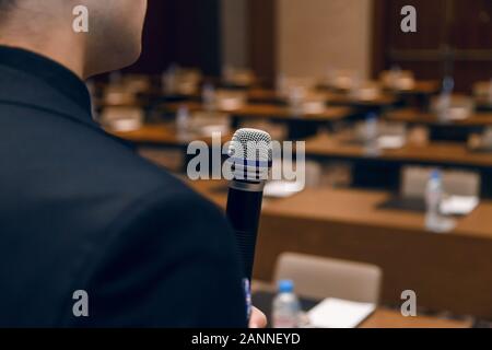 Mikrophon in der Hand der Mann im Anzug auf der Hintergrund der leeren Konferenzsaal. Generalprobe vor dem öffentlichen Sprechen Stockfoto