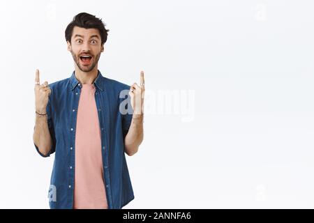 Charismatisch, gut aussehenden bärtigen Kerl mit Bart amüsiert, begeistert und überrascht, sah super Promo, nach oben gerichtet sein Freund coole Party zu zeigen. Thri Stockfoto