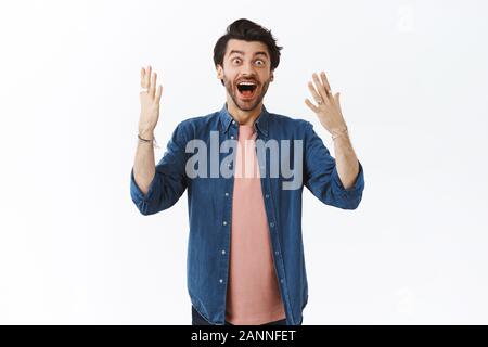 Emotionale, aufgeregt aussehenden bärtigen Kerl in trendigen Outfit, schütteln erhobenen Armen in Erstaunen und Freude, kann nicht glauben, dass Er gewann Preis, lächelnd und Suchen Stockfoto