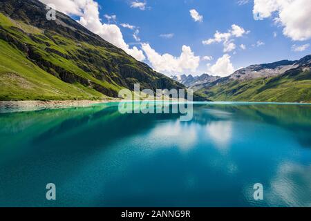 Berge spiegeln sich in den klaren blauen Wasser der See Lac de Moiry in den Walliser Alpen im Sommer mit einem schönen blauen Himmel und einige weiße cl Stockfoto