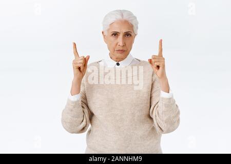 Enttäuscht, wütend düsteren ältere Dame mit grau gekämmte Haare, stirnrunzelnd und Schmollen, Pointing Finger an schrecklichen Banner, unbefriedigenden Szene, deman Stockfoto