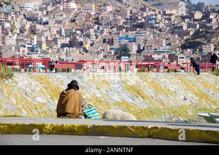 Der Mensch sitzt am Hafen von Puno mit seinem Lama, dem Titicacasee, Peru. Er wartet auf die Fähre zu den schwimmenden Inseln. Stockfoto