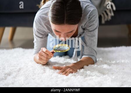 Junge weibliche Blick auf Teppich mit Lupe Stockfoto