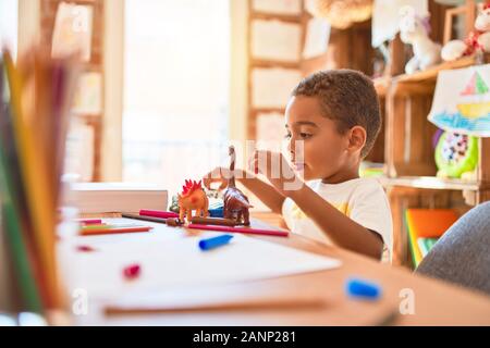 Schöne afrikanische amerikanische Kleinkind spielen mit Dinosaurier Spielzeug auf dem Schreibtisch im Kindergarten Stockfoto