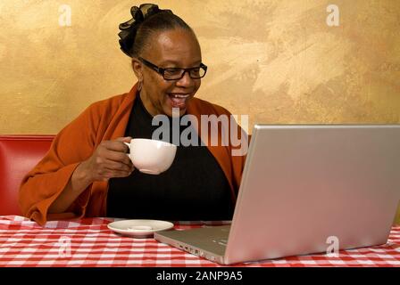 Eine Frau, die auf einem Laptop in einem Internetcafé eine Tasse Kaffee trinkt Stockfoto