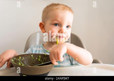 Kleiner Junge allein isst Püree aus einer Platte. Stockfoto