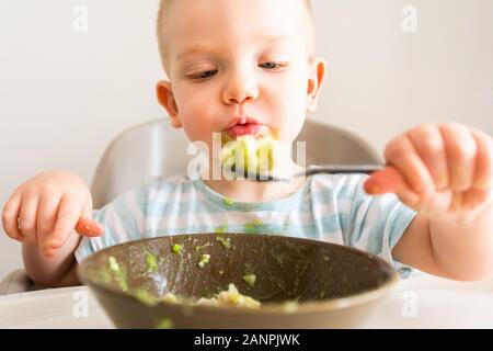 Kleiner Junge allein isst Püree aus einer Platte. Stockfoto