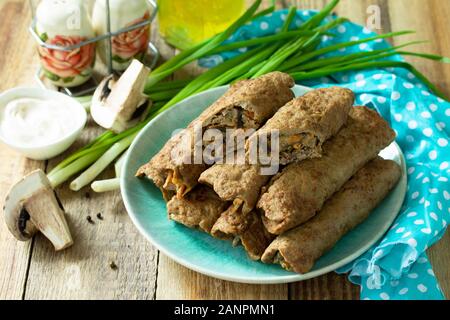 Das Konzept der ein gesundes Frühstück oder einen Snack. Fleisch, Leber Pfannkuchen gefüllt mit Pilzen und Gemüse in einer Platte auf rustikalen Holztisch. Stockfoto