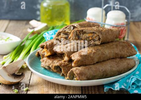 Das Konzept der ein gesundes Frühstück oder einen Snack. Fleisch, Leber Pfannkuchen gefüllt mit Pilzen und Gemüse in einer Platte auf rustikalen Holztisch. Stockfoto