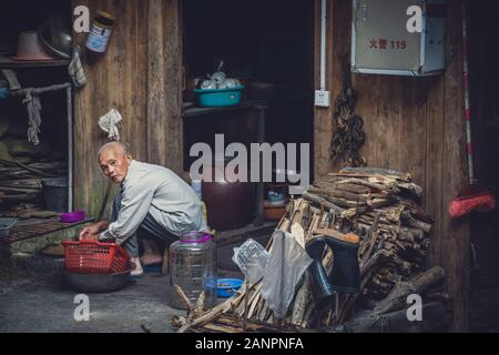 Pingan, China - August 2019: armen alten Mann tun Haus Aufgaben außerhalb seiner Holzhütte in Ping ein Dorf Longji Reisterrassen, Guangxi Provinz Stockfoto