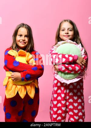 Kinder mit glücklichen Gesichtern halten Sie die grüne und die gelbe Sonne Kissen. Kindheit und Freundschaft Konzept. Mädchen mit losen Haare Hug ihre Kissen. Freunde in Pink polka gepunktete Schlafanzug auf rosa Hintergrund isoliert Stockfoto