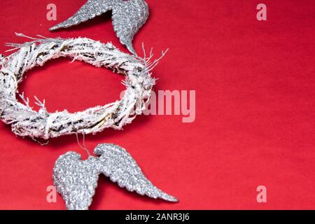 Eine Tür Kranz aus Zweigen verziert mit künstlichen Schnee. In der Nähe befinden sich Engel Flügel der silberne Farbe. Alles steht auf einem roten Hintergrund mit einem Platz f Stockfoto