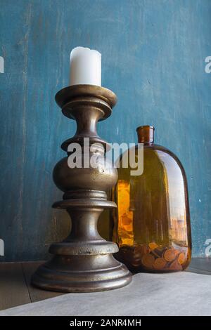 Große braune Glas Glas mit Münzen und massive Kerzenhalter mit weiße Kerze an es auf Blau schäbig Wand Hintergrund, Konzept der Einsparungen, Handel, Einsparungen Stockfoto