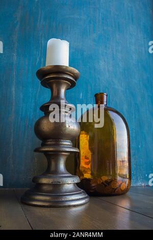 Große braune Glas Glas mit Münzen und massive Kerzenhalter mit weiße Kerze an es auf Blau schäbig Wand Hintergrund, Konzept der Einsparungen, Handel, Einsparungen Stockfoto