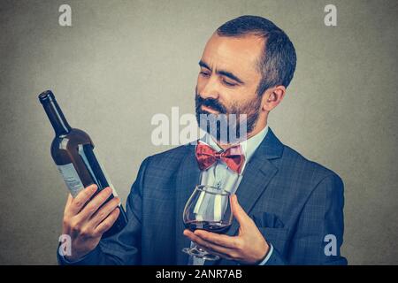 Ein Mann mit einem Glas Wein Holding, eine Flasche suchen, lesen Sie die Informationen über Sie. Gemischte Rasse bearded Modell auf grauem Hintergrund. Horizo Stockfoto