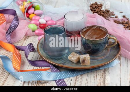 Traditionellen türkischen Kaffee in Porzellan Schale setzen, ein Glas Wasser und türkischem Honig, bunte Mandel Bonbons auf der Oberfläche mit Kaffeebohnen. Ein Fest (f Stockfoto