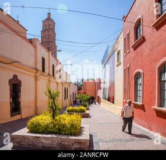 Dolores Hidalgo, Guanajuato, Mexiko - November 25, 2019: Der Mann, der zu Fuß auf Relox Straße, mit einem wandbild an der Wand und den Kirchturm im Hintergrund Stockfoto