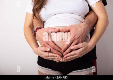 Zugeschnittenes Bild der schönen schwangeren Frau und ihrem stattlichen Mann umarmen den Bauch Stockfoto