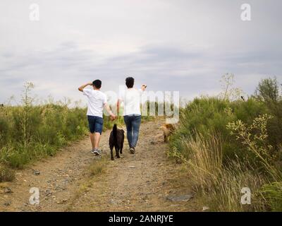 Junge homosexuelle Paare zu Fuß durch die Hand mit zwei Hunden, Tandil, Buenos Aires, Argentinien. Stockfoto
