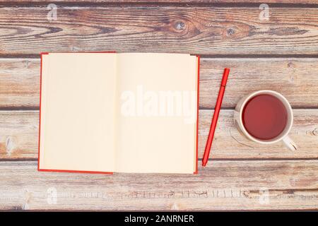 Öffnen Sie rotes Buch und eine Tasse Tee auf dem Tisch Stockfoto
