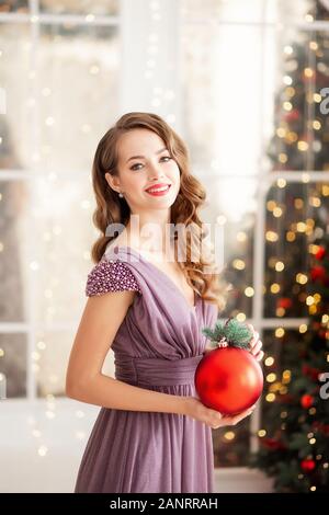 Junge Frau mit Make-up und Frisur hält Geschenk Bälle für die Einrichtung der Weihnachtsbaum. Konzepterstellung für Urlaub neues Jahr Stockfoto