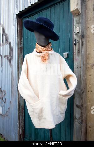 Eine Schaufensterpuppe in einem weißen Strickjacke, ein gelbes Halstuch und einem blauen Hut mit breiter Krempe steht auf der Straße in der Nähe ein Geschäft mit antiken Dingen. Stockfoto