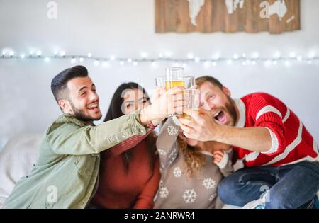 Eine Gruppe von Freunden jubelt zu Hause bei der weihnachtsfeier mit Bier - Junge Leute haben zusammen Spaß am Trinken und Lachen - Urlaub, Jugend-Lifestyle, Freund Stockfoto