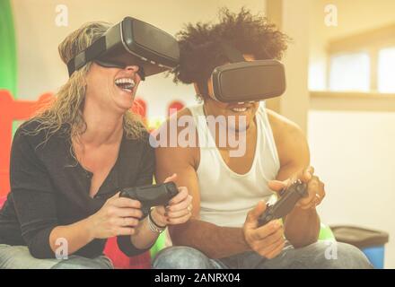 Fröhliches Vielvölkerpaar spielt Videospiele virtuelle Reality-Brille im Spielplatzcenter - Fröhliche Leute, die mit vr-neuer Technologie Spaß haben - Weich Stockfoto