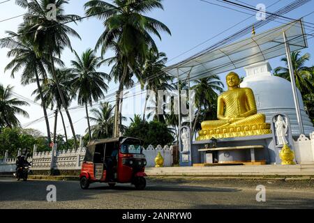 Galle, Sri Lanka - Januar 2020: Ein Tuk Tuk, das am 15. Januar 2020 in Galle, Sri Lanka, vor der Buddha-Statue auf einer Straße in Galle vorbeigeht. Stockfoto