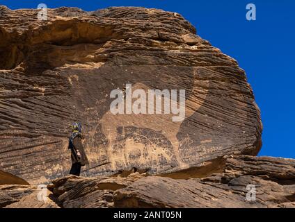 Touristische stand vor einer lebensgroßen Kamel petroglyph auf einen Felsen, der Provinz Najran, Thar, Saudi-Arabien Stockfoto