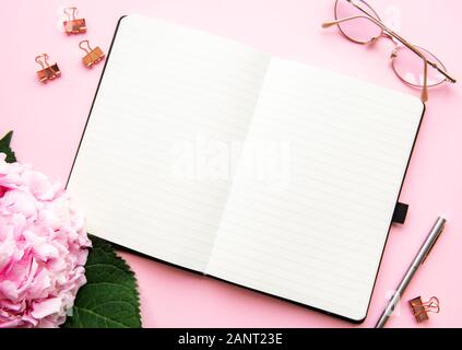 Home office Arbeitsbereich, Notebook, pink hydrangea und Zubehör auf rosa Hintergrund. Flach. Stockfoto