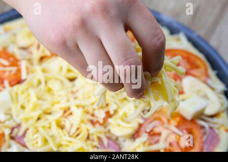 Die Hand der Frau besprüht Pizza mit Mozzarella, Tomaten, Salami und Bananen auf dem sehr Vorbereitung der Zersetzung Stockfoto