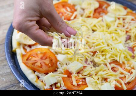 Die Hand der Frau besprüht Pizza mit Mozzarella, Tomaten, Salami und Bananen auf dem sehr Vorbereitung der Zersetzung Stockfoto