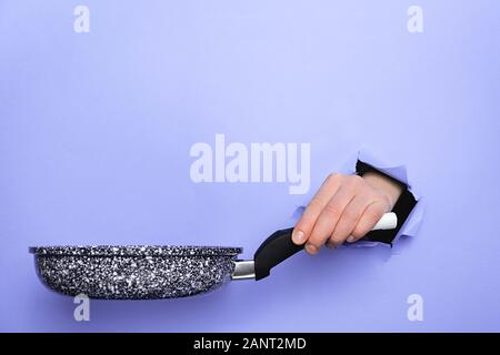 In der Nähe der weiblichen Hand Pfanne durch Papierreste violetten Hintergrund. Küchengeräte Konzept. Kopieren Sie Platz für Werbung Stockfoto