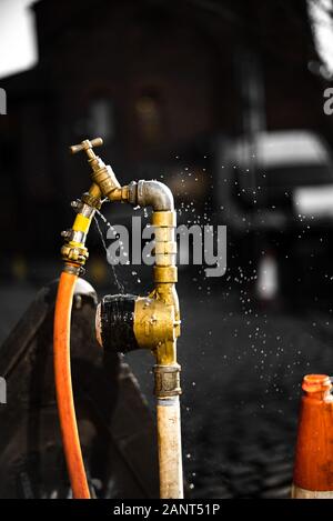 Undichte Hydranten Sprühwasser Closeup UK Stadtschlauch gelb Gefrierzeit dunkler Hintergrund isolierter Mitarbeiter Wasserhahn Bokeh scharfes Objekt main Stockfoto