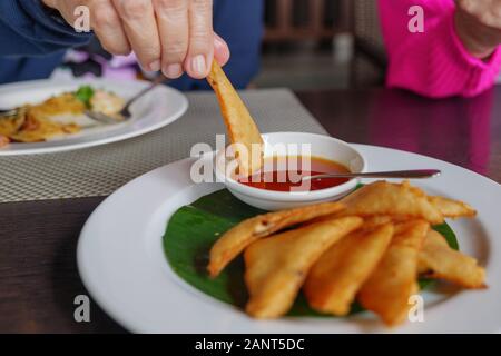 Fokussieren Sie den Blick auf die Hand, und tauchen Sie ein Stück Dreieck knuspriger Garnelen und Pilze umhüllt, eine Art thailändisches Süßfleisch, in Passionsfruchtsauce auf der Seite. Stockfoto