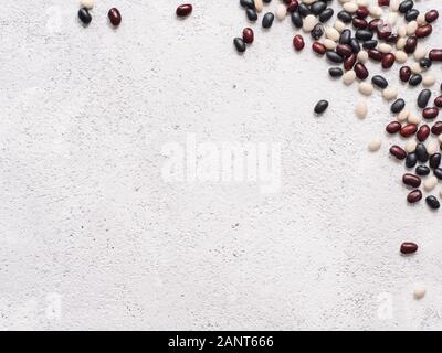 Blick von oben auf die Rohstoffe gemischt Bohnen auf Grau cemeent Hintergrund. Der uncoocked schwarze, rote und weiße Bohnen mit Kopie Raum gemischt. Essen Hintergrund. Vegan protein Konzept. Flach Stockfoto