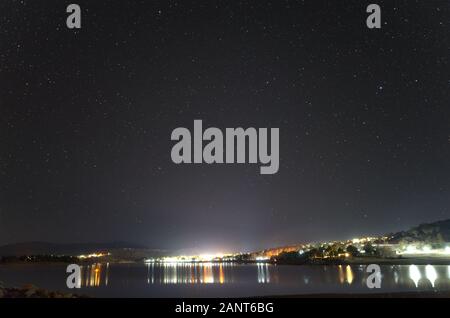 Sterne über einen blattlosen Baum am Ufer des Lake Jindabyne Jindabyne mit der Stadt im Hintergrund Stockfoto